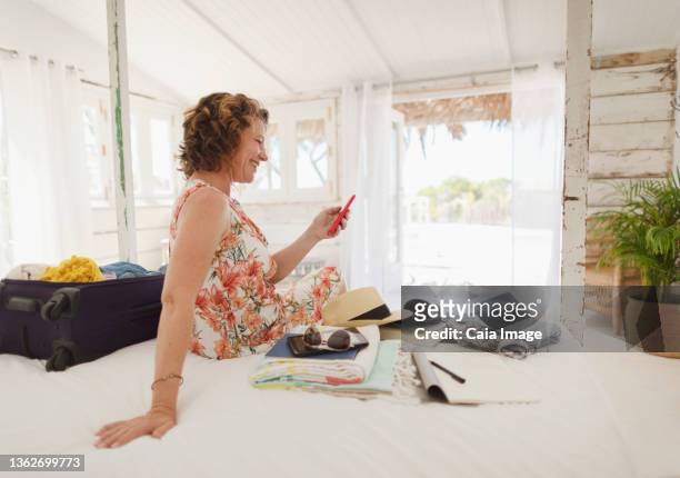 woman with smart phone unpacking suitcase on beach hut bed - beach hut fotografías e imágenes de stock