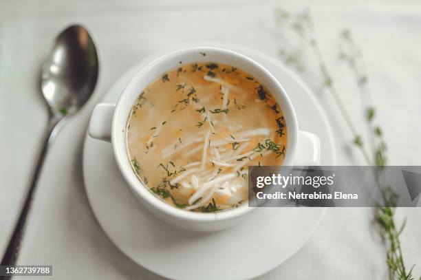 homemade chicken soup with noodles and herbs in a beautiful white plate on a white table, white background. healthy warm food. homemade food. - chicken soup stock pictures, royalty-free photos & images