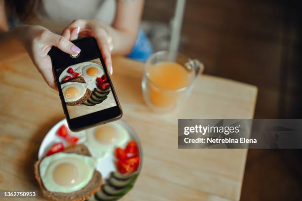 a food blogger uses his smartphone to take pictures of his breakfast on a wooden table to share it on social networks. black smartphone - camera screen stock-fotos und bilder