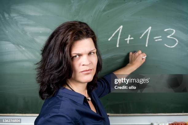 female teacher pointing at the blackboard, looking serious - educational subject stock pictures, royalty-free photos & images