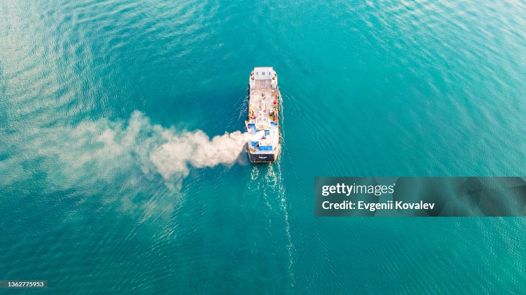 Luftaufnahme eines Containerschiffes mit Fracht für ein Import-Export-Logistikunternehmen im Ozean. Rauch von einem Schiff, das im Ozean segelt