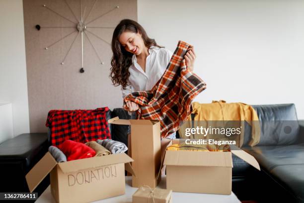 woman holding clothes with donate box in her room, donation concept - winter coats stockfoto's en -beelden