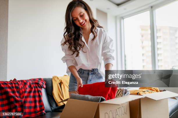 woman holding clothes with donate box in her room, donation concept - klädesplagg bildbanksfoton och bilder