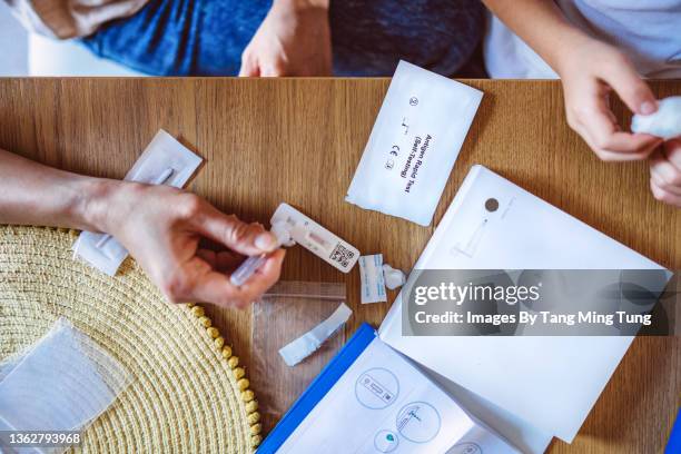 directly above view of mom using covid-19 rapid self-test kit for her kid at home - corona fotografías e imágenes de stock