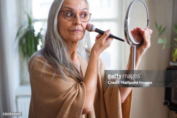 senior woman looking at mirror and applying make up at home, selfcare concept. - applying stock-fotos und bilder