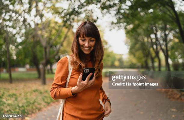 portrait of a beautiful mid adult woman with mobile phone standing outside in the city on autumn day. - slovakia town stock pictures, royalty-free photos & images