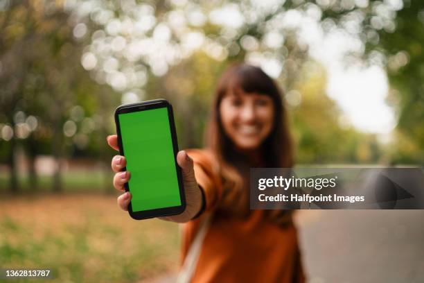 beautiful mid adult woman showing smart phone looking at camera outside in the city on autumn day. - showing phone stock pictures, royalty-free photos & images