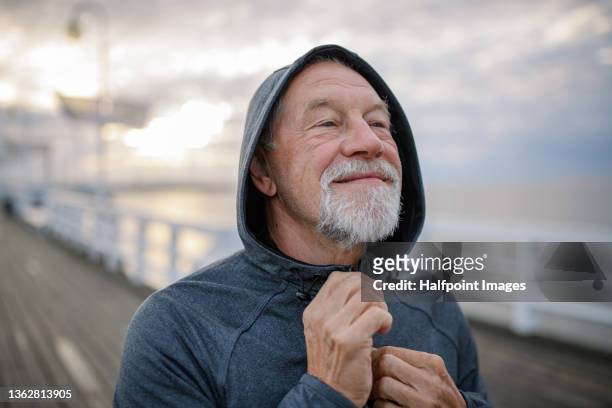 portrait of active senior man resting after doing exercise outdoors on pier by sea in early morning. - overcast portrait stock pictures, royalty-free photos & images