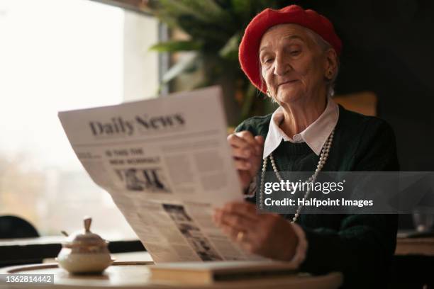 elegant senior woman reading newspaper and having coffee indoors in café. - senior women cafe stock pictures, royalty-free photos & images