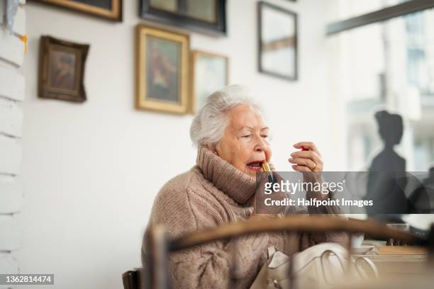 elegant senior woman, applying red lipstick indoors in cafeteria. - make up table stock pictures, royalty-free photos & images