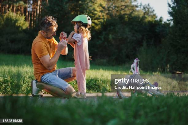 mature man applying bandage to his little daughter after fall from bike outdoors in park. - accident de transport photos et images de collection