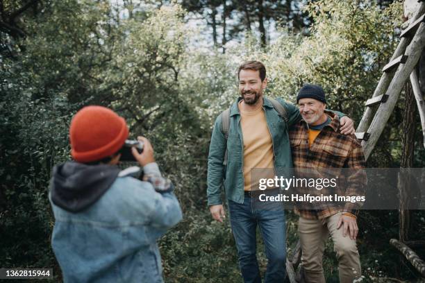 a small multiracial boy taking picture of father and grandfather in forest in autumn day. - boy taking picture in forest stock-fotos und bilder