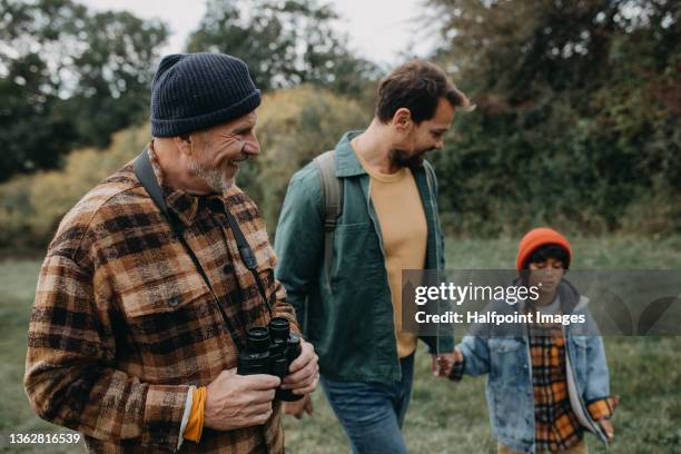 a small multiracial boy with father and grandfather walking in forest nature in autumn day - abuelos fotografías e imágenes de stock