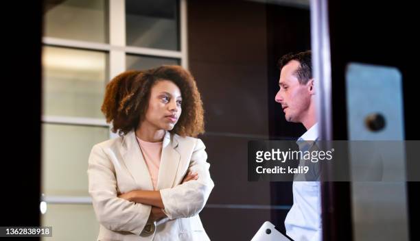 african-american woman talks with man in office lobby - angry coworker stock pictures, royalty-free photos & images