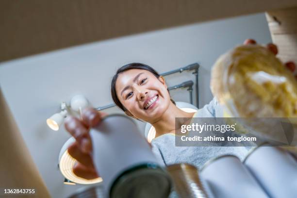 person woman receiving donation food box. female volunteer hands packing donation box with food items of staple products on wooden table. donate food delivery concept. donations grocery canned food. - cereal box stockfoto's en -beelden