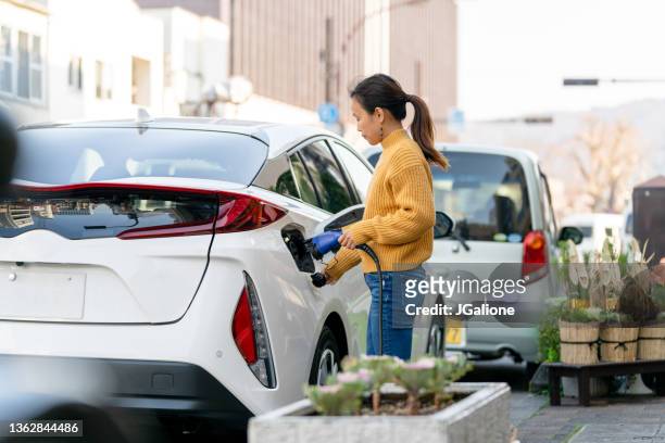 mujer medianamente adulta enchufando un coche eléctrico para cargar - cargar fotografías e imágenes de stock