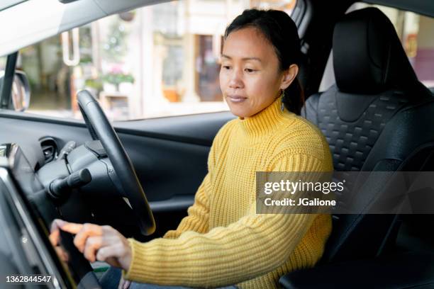 mid adult woman using touch screen in her electric car - tesla interior stock pictures, royalty-free photos & images