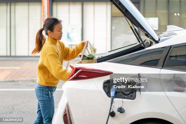 mid adult woman loading groceries into her electric car - hybrid car stockfoto's en -beelden