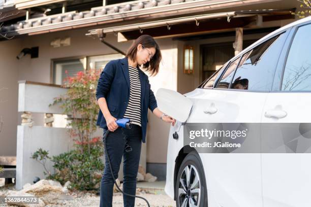 mid adult woman charging her electric car at home - electric car home stock pictures, royalty-free photos & images