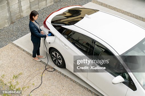 自宅で彼女の電気自動車を充電中の成人女性 自宅で彼女の電気自動車を充電中の成人女性