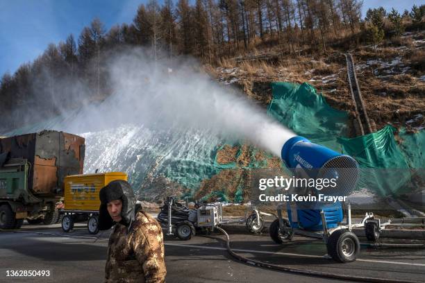 Workers stands next to a snow machine making artificial snow outside one of the athletes villages for the Beijing 2022 Winter Olympics before the...