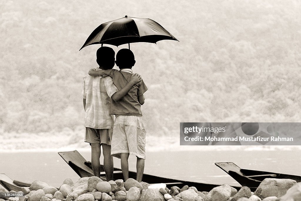 Two friends standing on river bank under umbrella