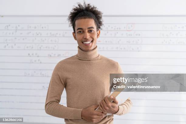 un maestro africano de pie en un aula vacía y sosteniendo libros - male professor with students fotografías e imágenes de stock