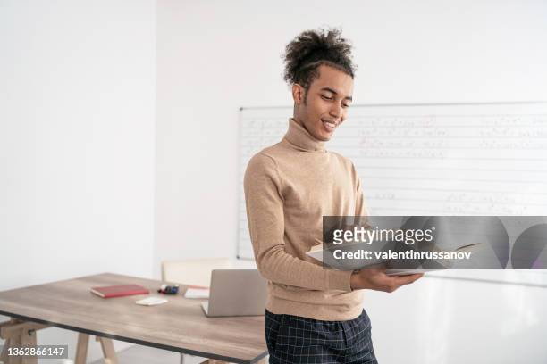 an african male teacher standing in an empty classroom and holding books - closing book stock pictures, royalty-free photos & images