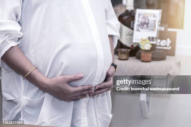 image of pregnant woman touching her belly with hands - umstandskleidung stock-fotos und bilder