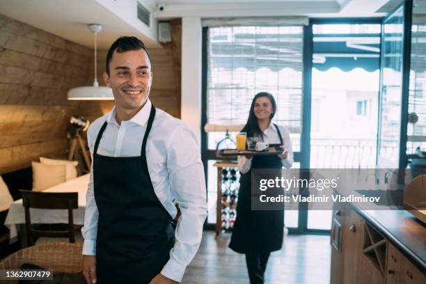 fröhlicher junger kellner und seine kollegin bei der arbeit im restaurant - catering stock-fotos und bilder