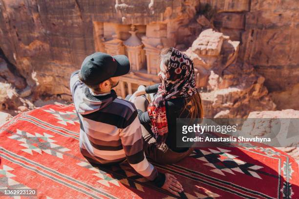 happy male and female travelers contemplating the scenic view of ancient petra from mountain top - jordan pic stock pictures, royalty-free photos & images