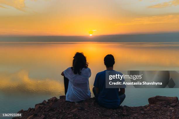 glückliche junge frau und mann, die den malerischen sonnenuntergang über dem toten meer in jordanien betrachten - jordan middle east stock-fotos und bilder