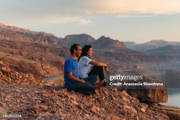 glückliche junge frau und mann, die den malerischen sonnenuntergang über dem toten meer in jordanien betrachten - totes meer stock-fotos und bilder