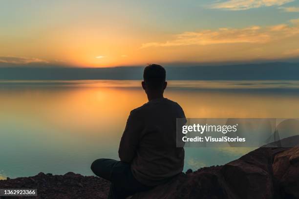 hombre joven contemplando la pintoresca puesta de sol sobre el mar muerto en jordania - escena de tranquilidad fotografías e imágenes de stock