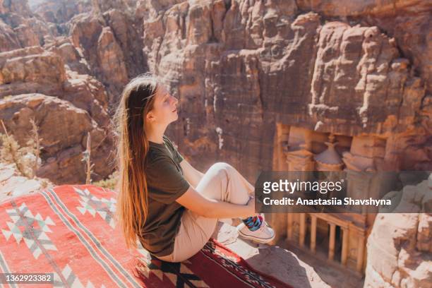 female traveler contemplating the scenic view of ancient petra from mountain top - international landmark stock pictures, royalty-free photos & images
