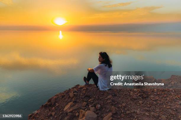 silhouette einer frau, die den malerischen sonnenuntergang über dem toten meer in jordanien betrachtet - jordan middle east stock-fotos und bilder