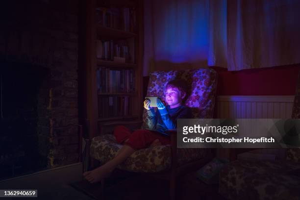 a young boy sat on a sofa in a living room at night, his face lit up by the smartphone he's looking at - sattel bildbanksfoton och bilder