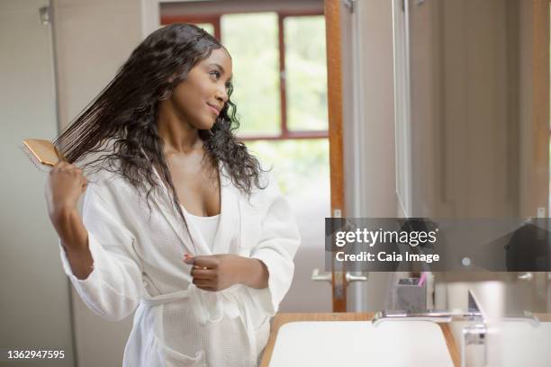 beautiful young woman brushing hair in bathroom mirror - haare kämmen stock-fotos und bilder