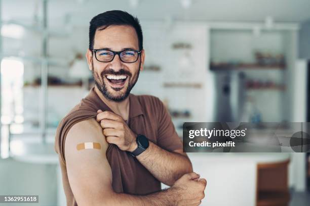 smiling man showing covid-19 vaccination - arms stockfoto's en -beelden