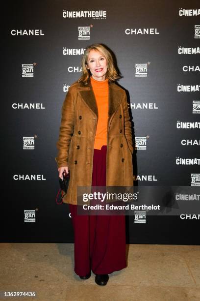 Marianne Basler wears a brown long winter leather aviator coat with fluffy inner lining, an orange wool turtleneck ribbed pullover, red burgundy wide...