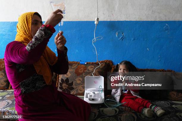 Aisha Mohammed Ali a mother of five who is a refugee from Aleppo, Syria, assists one of her daughters, who has asthma, on January 5, 2022 in Tripoli,...