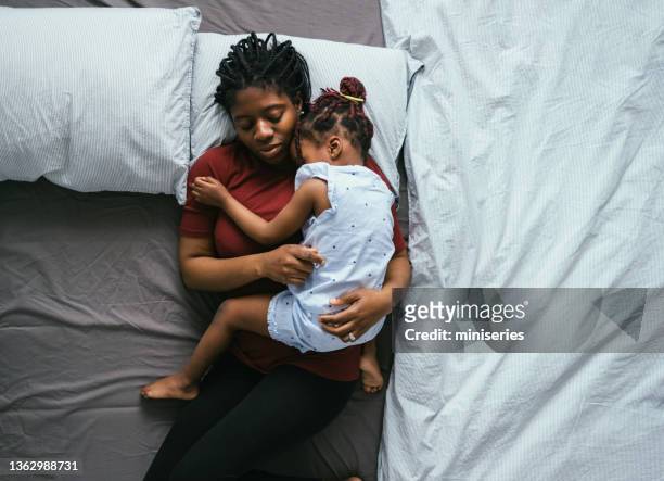 top view of beautiful mother with little daughter sleeping in bed - black child stockfoto's en -beelden