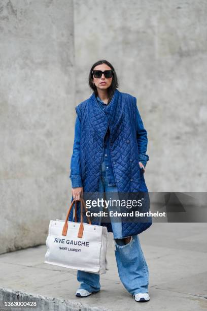Gabriella Berdugo wears sunglasses, a long blue quilted / padded sleeveless winter coat from Copenhagen Muse, a blue denim shirt from Wrangler,...