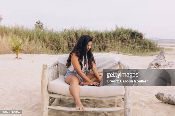side view of a latina woman using a computer while she,´s sitting on the beach chair with bushes on the back - businesswoman barefoot stock-fotos und bilder