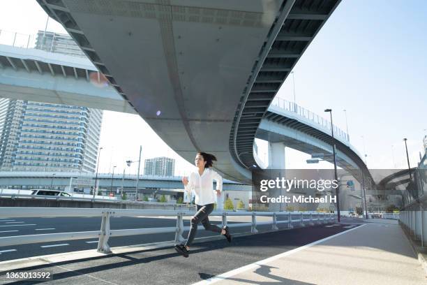 young fit woman running under a highway overpass  with sportswear middle of the city - leap forward stock pictures, royalty-free photos & images
