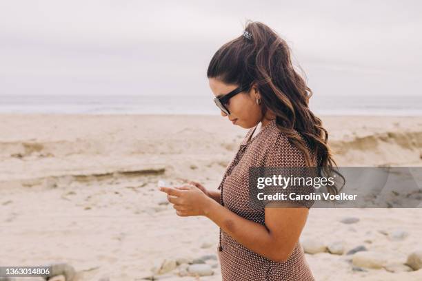 standing women on the beach concentrated on phone - beach goers stock pictures, royalty-free photos & images