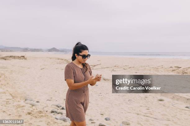 standing woman on the beach using a mobil phone - beach goers stock pictures, royalty-free photos & images