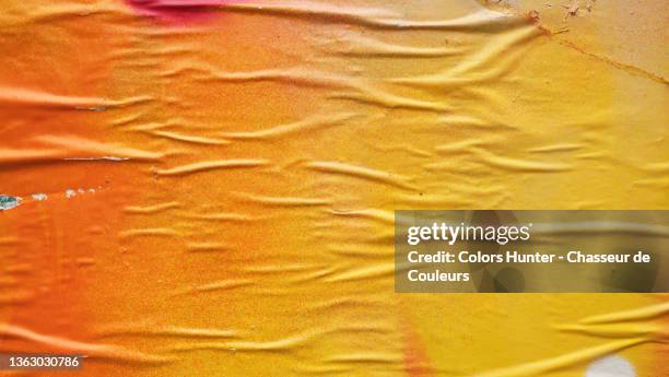 yellow and orange paper stuck and wrinkled on a wall in paris - le mur photos et images de collection