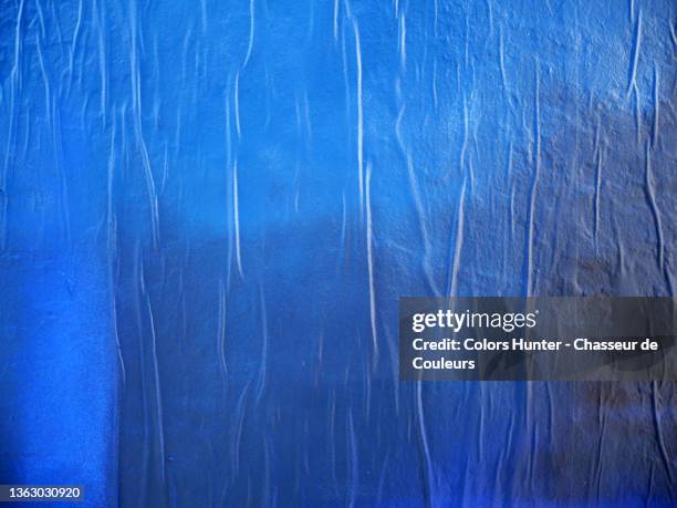 blue and black paper stuck and wrinkled on a wall in paris - poster wall stock-fotos und bilder