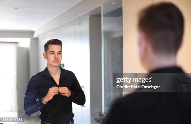 a young man buttoning up his shirt in front of the mirror. - form fitted stock pictures, royalty-free photos & images